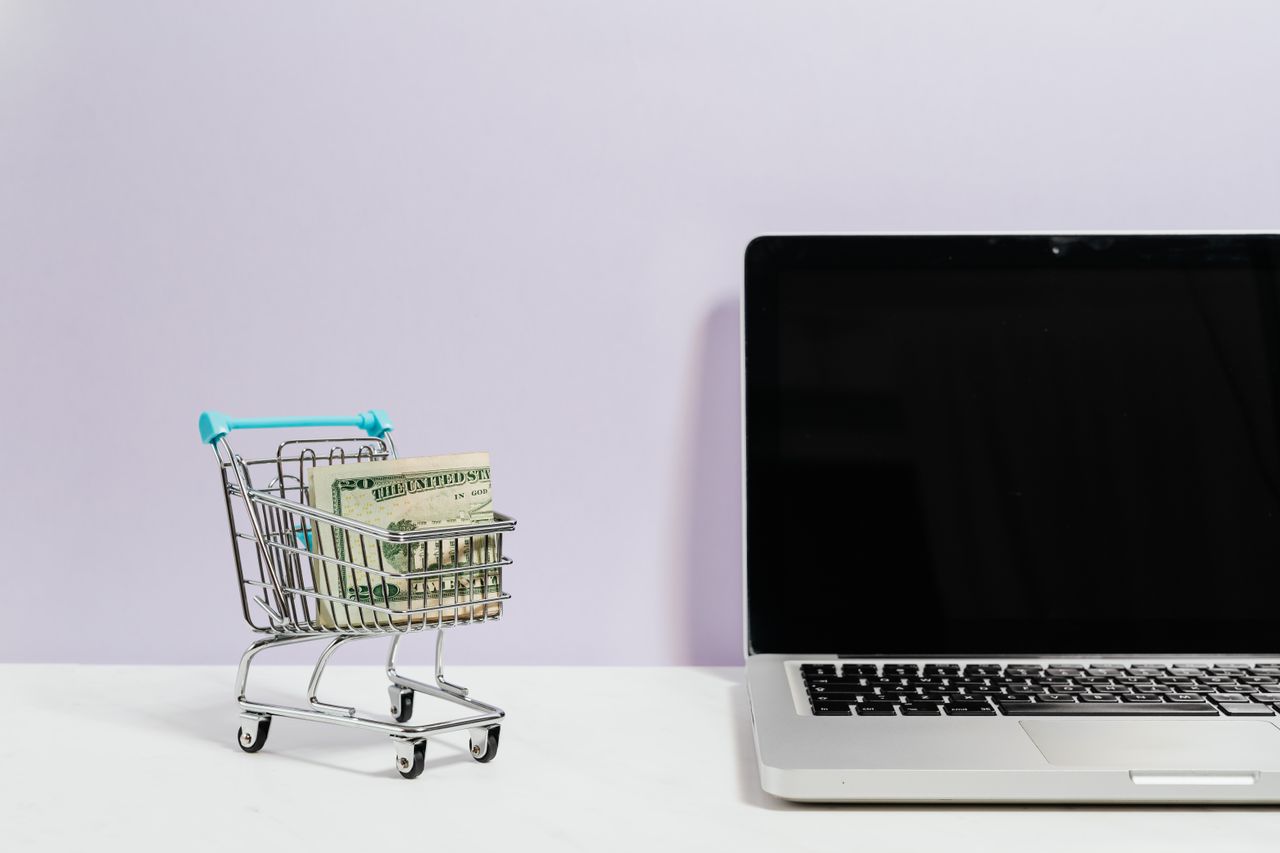 Crafting Captivating Headlines: Your awesome post title goes here Mini shopping cart with cash beside a laptop, symbolizing online shopping and e-commerce.