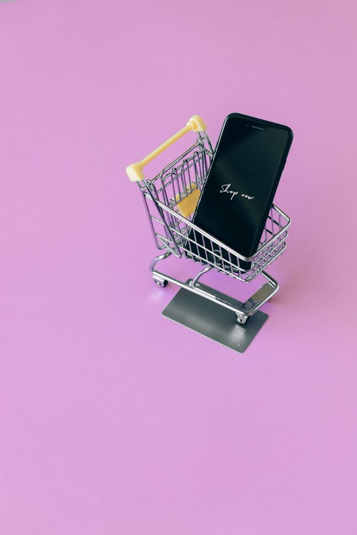 Mastering the First Impression: Your intriguing post title goes here Mobile phone in mini cart on pink surface, symbolizing online shopping.